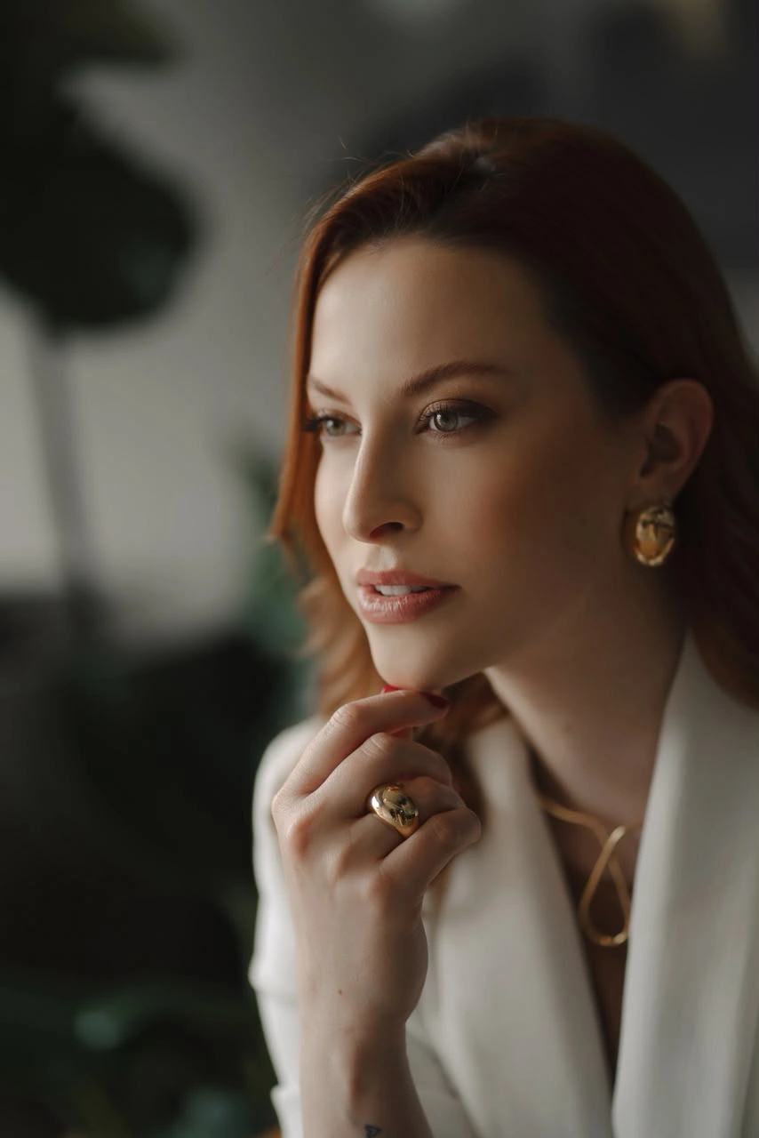 Fotografia real de Bruna Cornelius com blazer claro, olhando para o lado e com a mão próxima ao rosto.